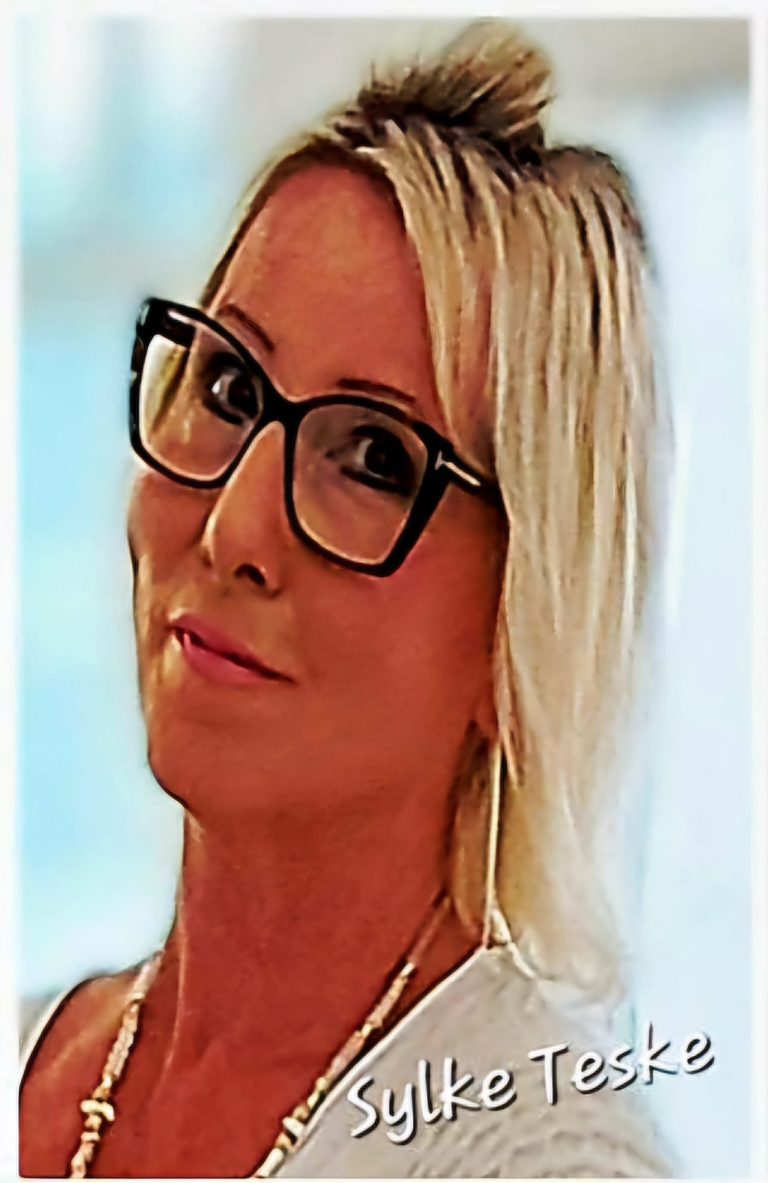 Frau mit blonden Haaren und Brille, lächelt freundlich in die Kamera.