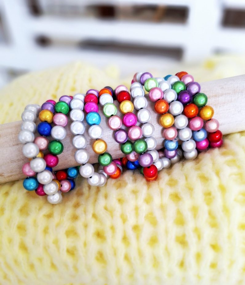Bunte Perlenarmbänder in verschiedenen Farben auf einem Holzstab.