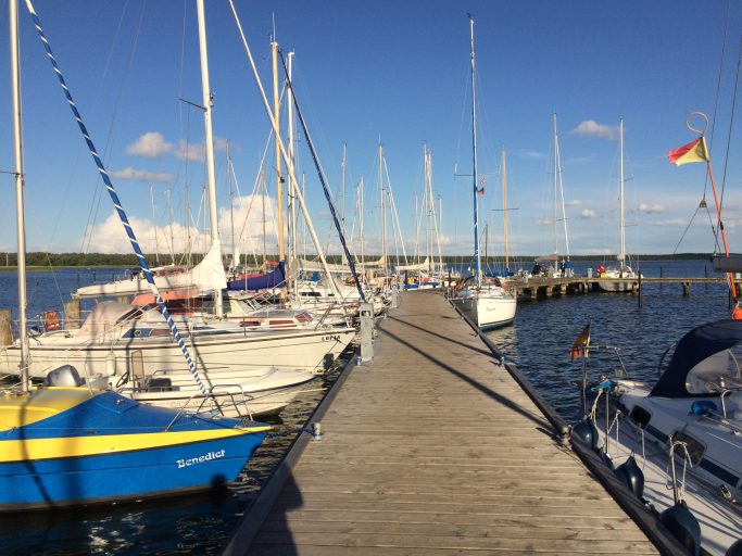 Segelboote liegen an einem Steg am Wasser unter blauem Himmel.