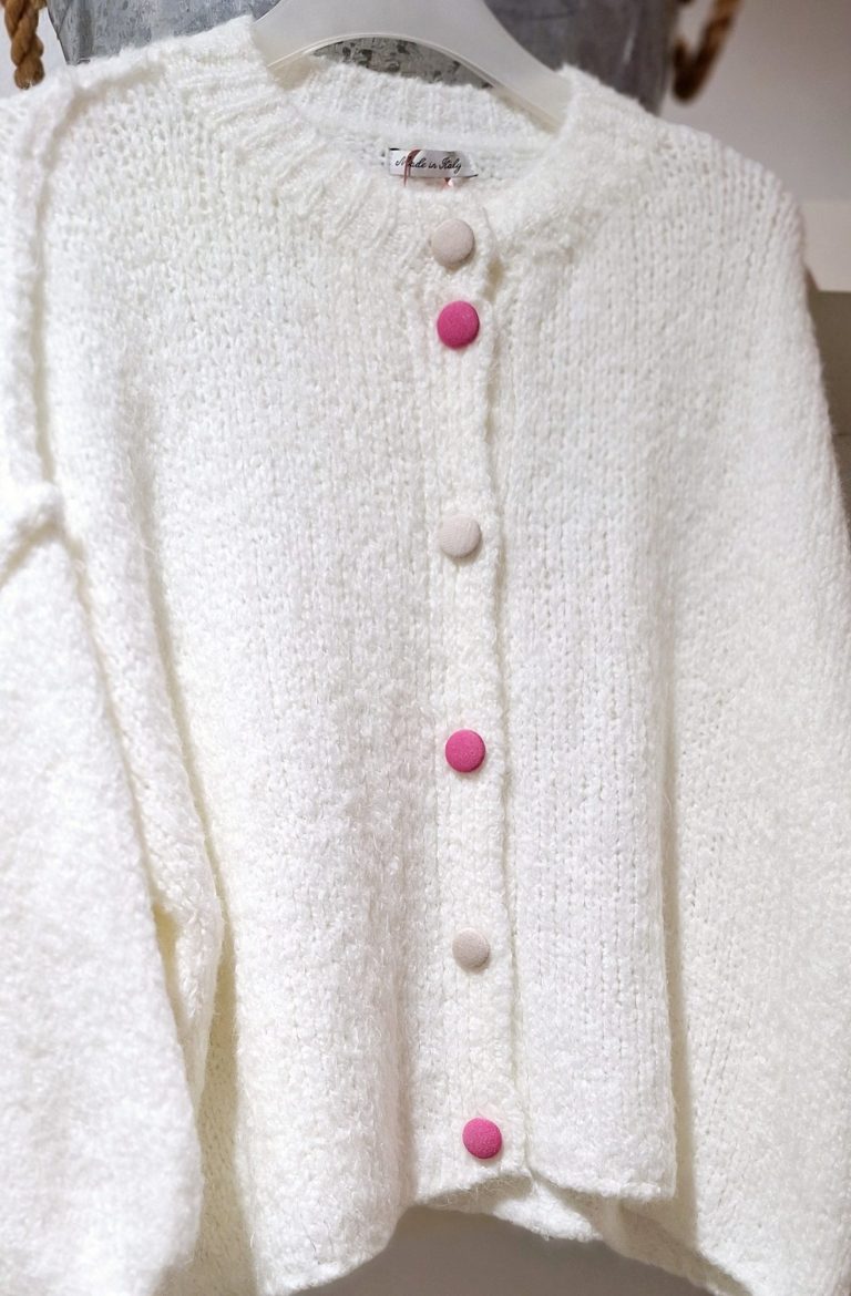 Beige Strickjacke mit verschiedenen pinken und sandfarbenden Knöpfen, auf einer Schneiderpuppe.