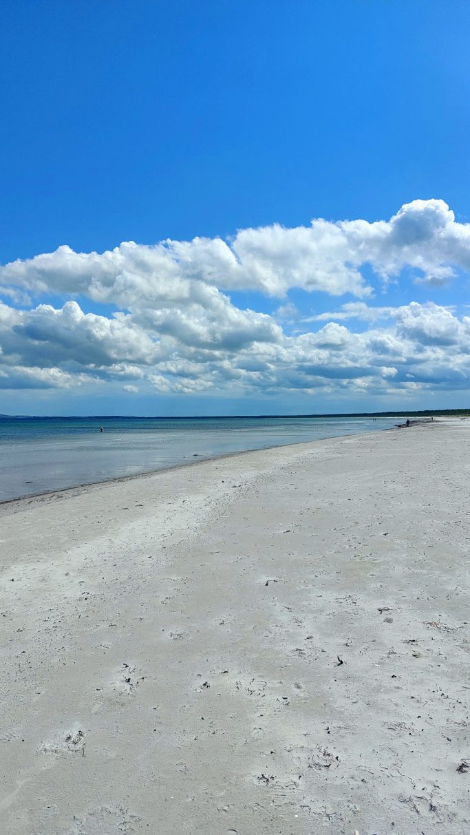Ein heller Sandstrand mit sanften Wellen und bewölktem Himmel.