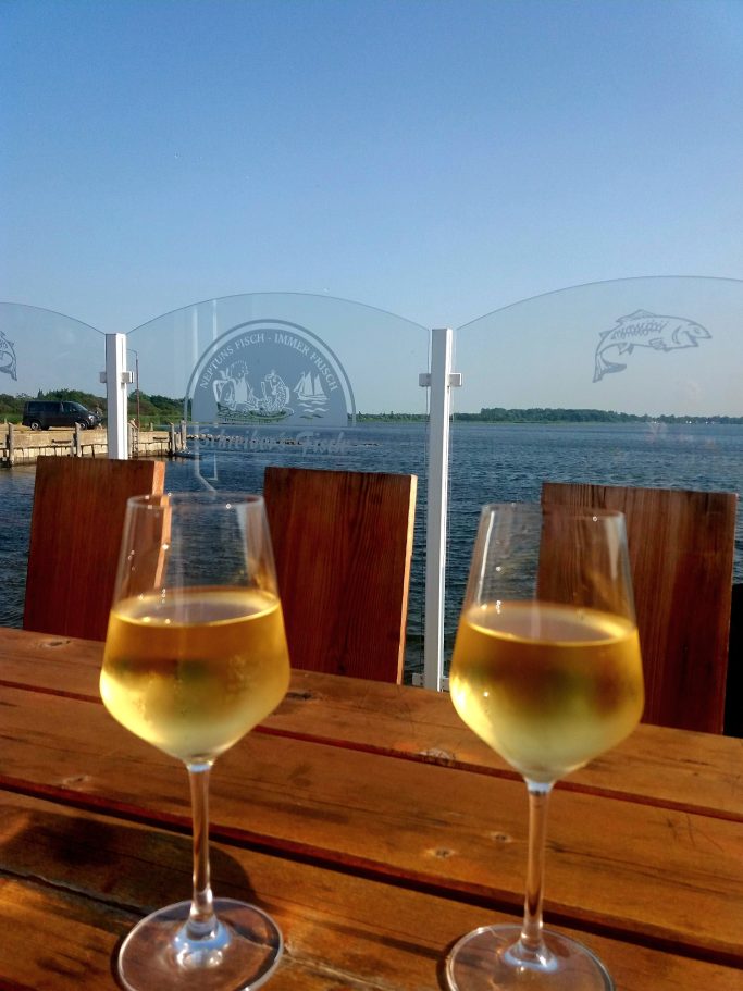 Zwei Weingläser auf einem Tisch mit Blick auf das Wasser und eine klare blaue Himmel.