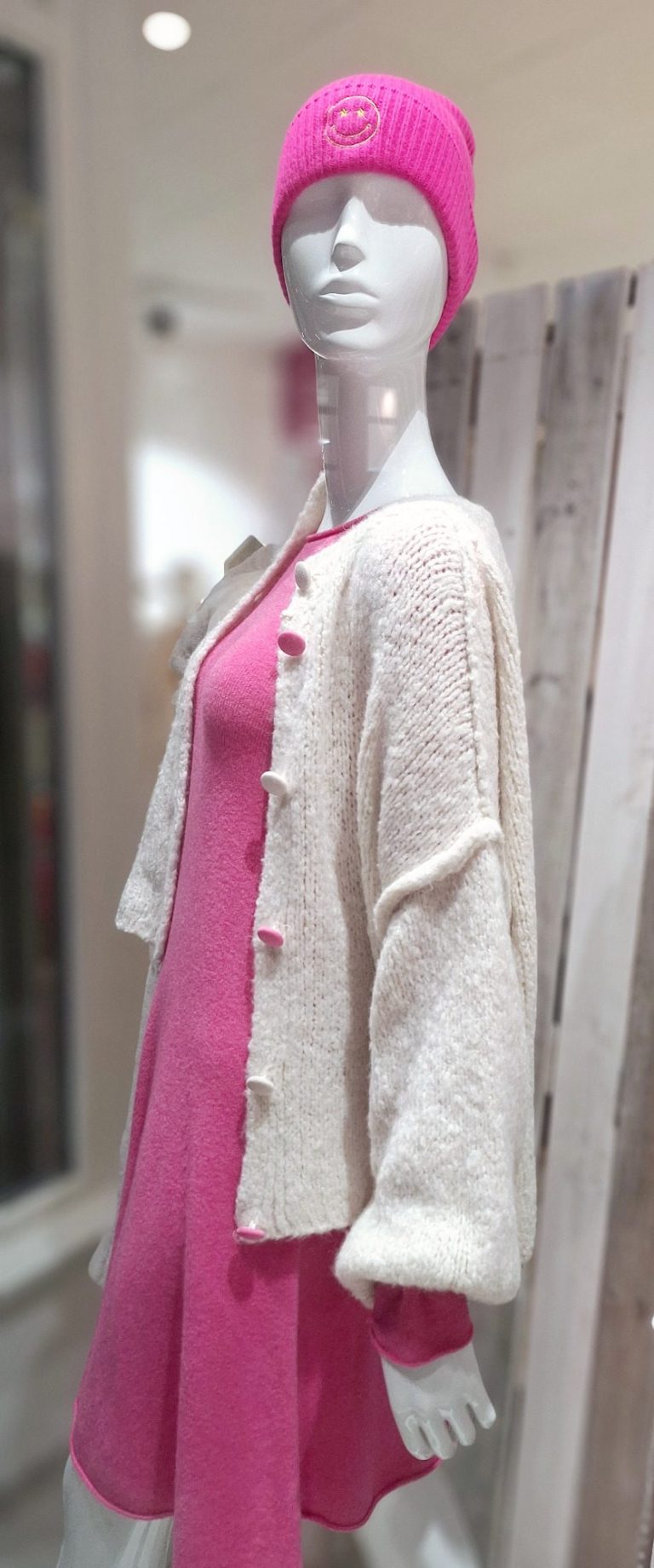 Damenpuppe in pinkem Kleid und wollweiße Strickjacke mit Mütze in einem Geschäft.