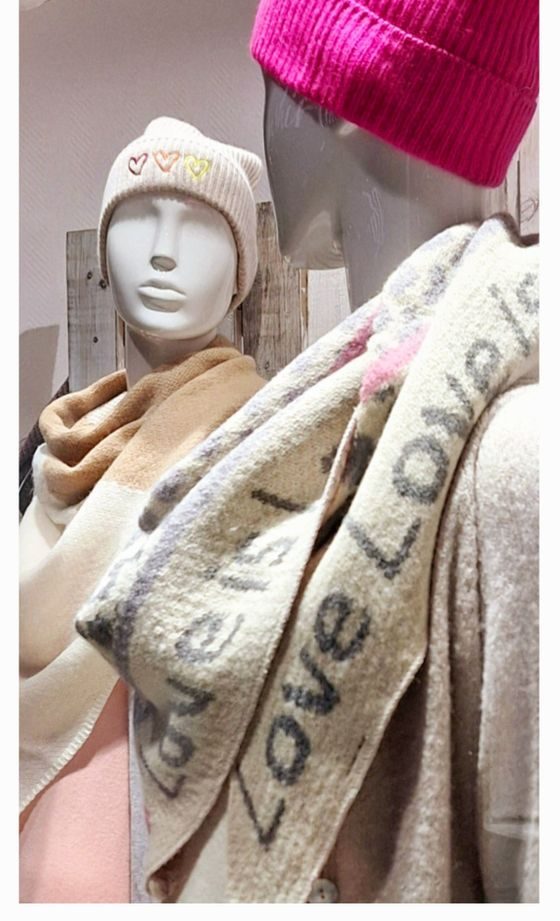 Zwei Schaufensterpuppen tragen Mützen und Schals in sanften Farben.