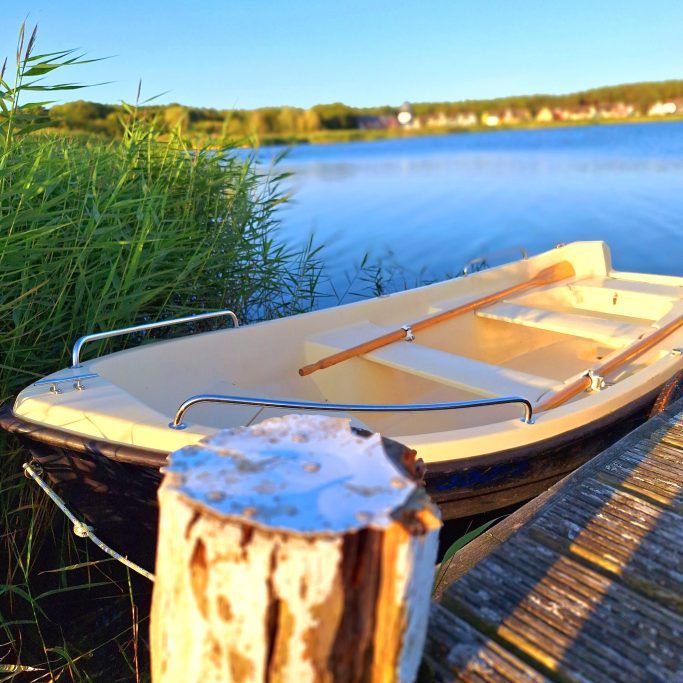Ein kleines Boot liegt am Ufer eines ruhigen Gewässers, umgeben von grünen Pflanzen.
