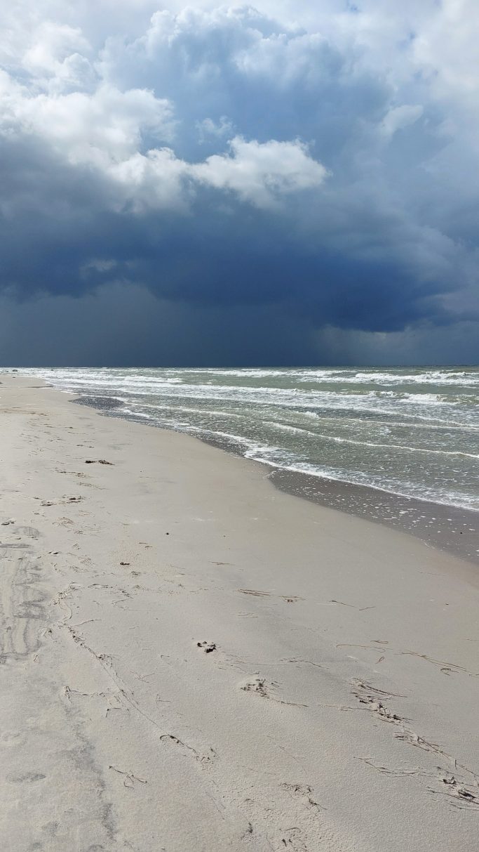 Stürmischer Strand mit Wellen und dunklen Wolken am Himmel.