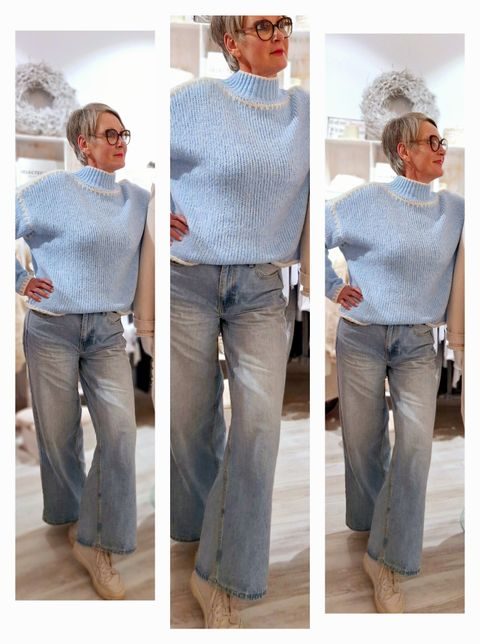 Eine Person mit kurzem, grauem Haar trägt einen blauen Pullover und weite, stylische Jeans.