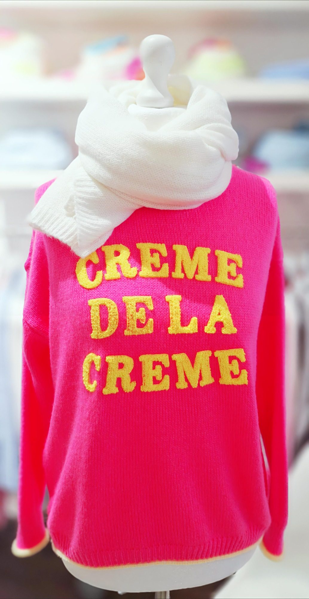 Rosa Pullover mit gelbem Schriftzug "CREME DE LA CREME" und weißem Schal.