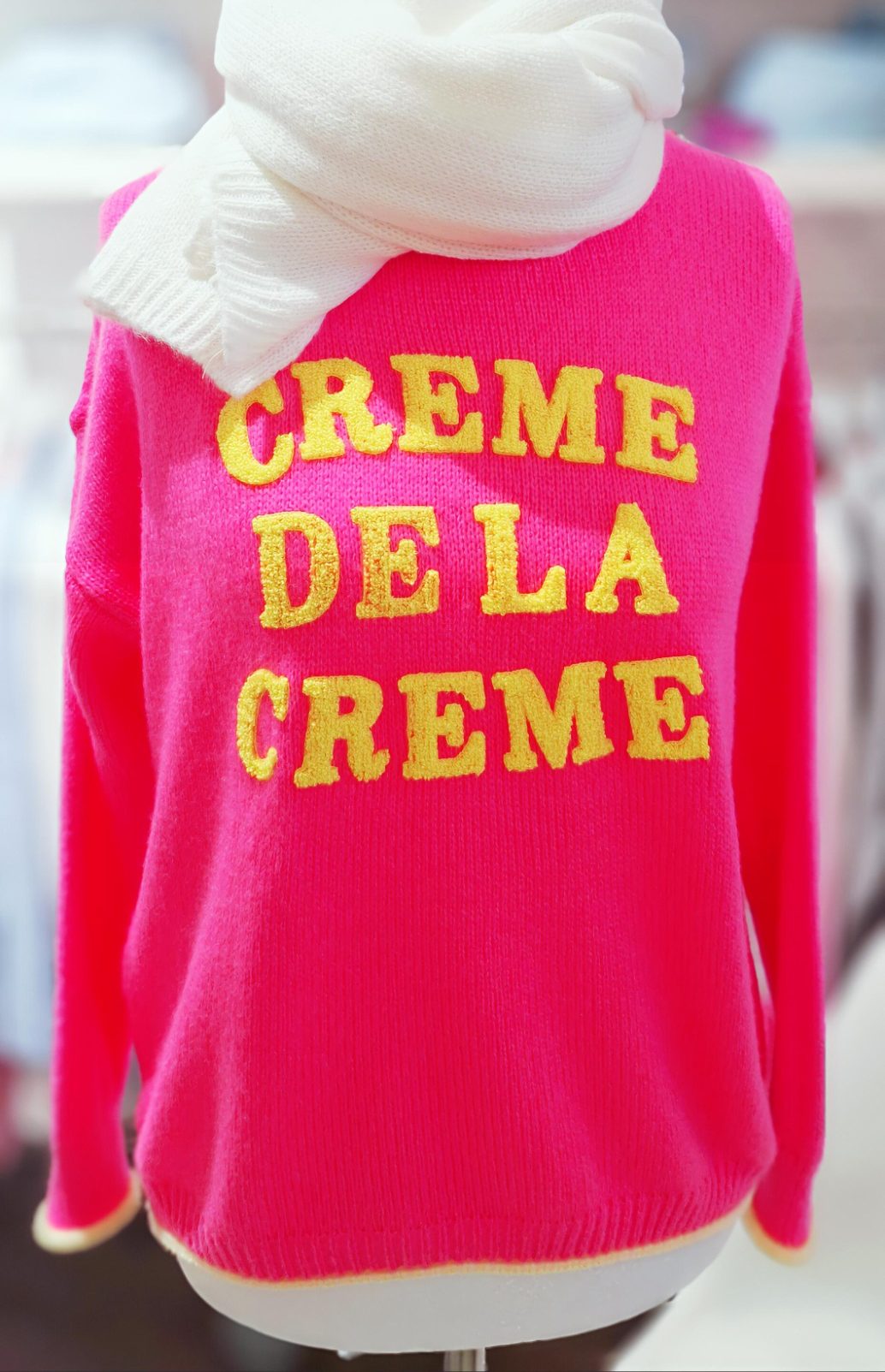 Rosa Pullover mit gelbem Schriftzug "CREME DE LA CREME" und weißem Schal.