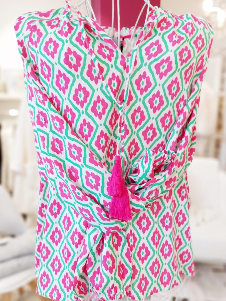 Fuchsia und grüne Bluse mit geometrischem Muster und pinkem Quastenanhänger.