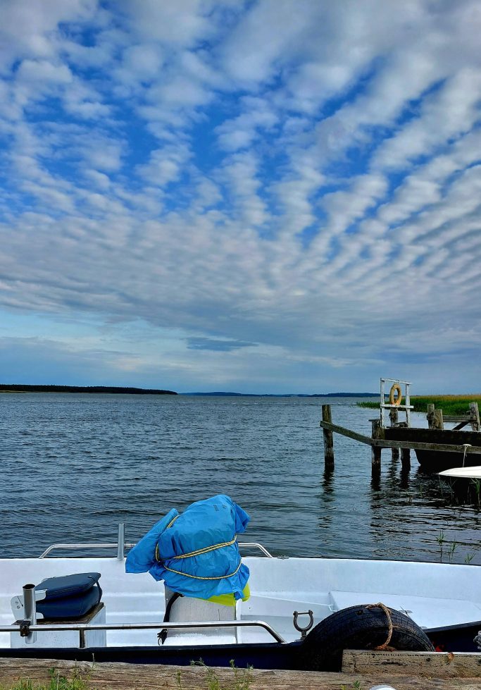 Ein Boot liegt am Ufer, während Wolken über dem Wasser ziehen.