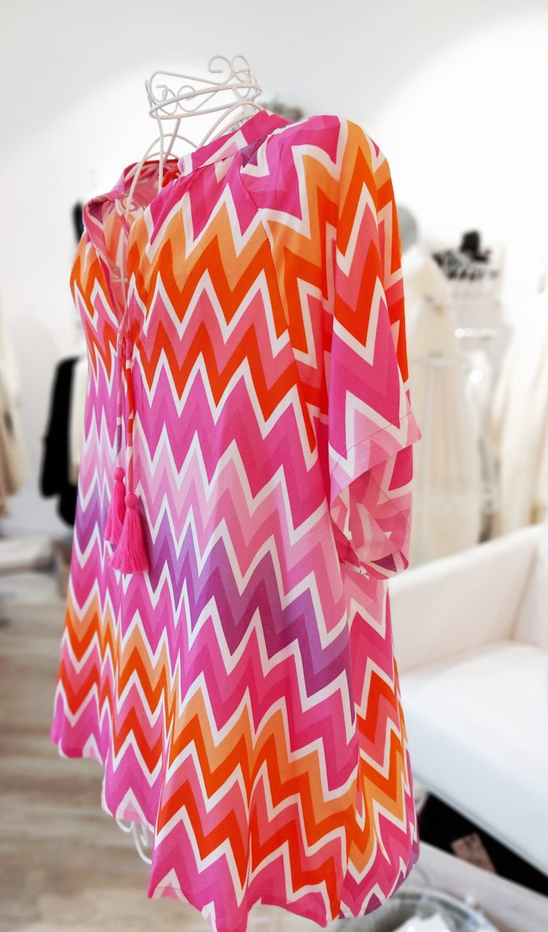 Farbenfrohes, gestreiftes Kleid in Rosa, Orange und Weiß, ausgestellt in einem Geschäft.
