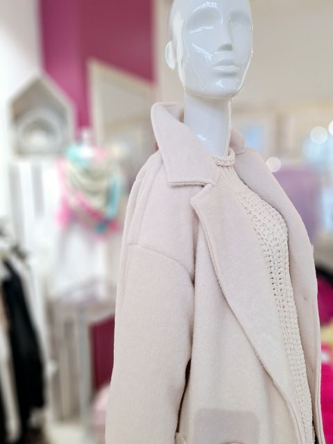 Beige Mantel an einer Schaufensterpuppe vor einem pinken Hintergrund.