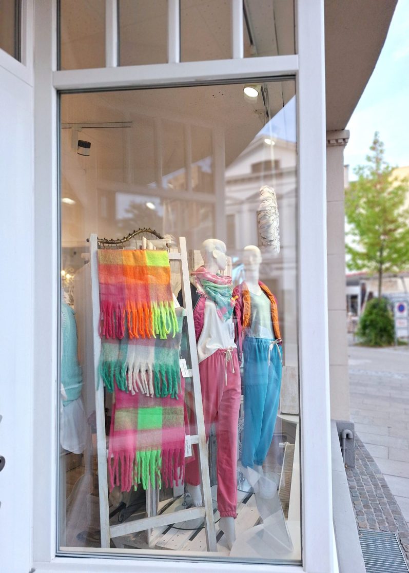 Schaufenster mit bunten Schals und Schaufensterpuppen in modischer Kleidung.