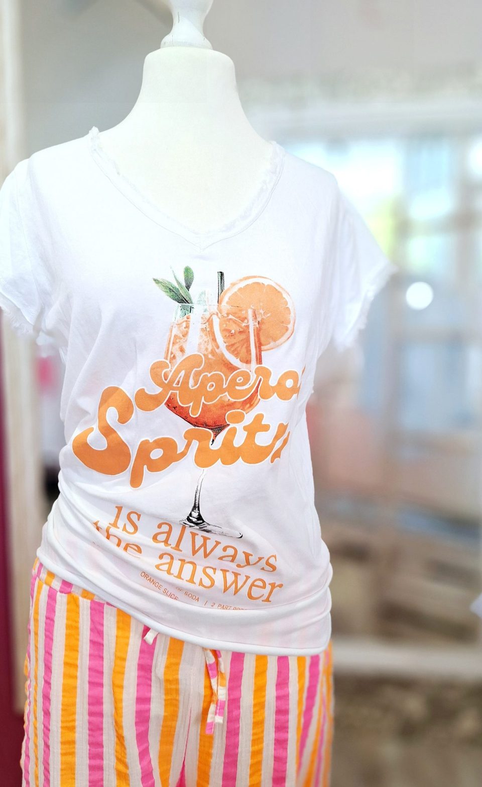 Weißes T-Shirt mit orangem Aufdruck und farbigen gestreiften Hosen.