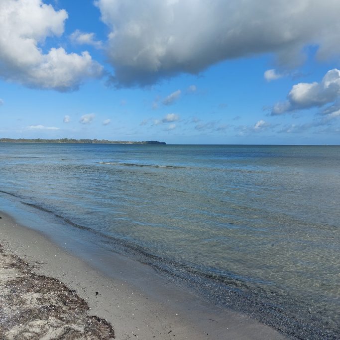 Ruhiger Strand mit sanften Wellen und bewölktem Himmel im Hintergrund.