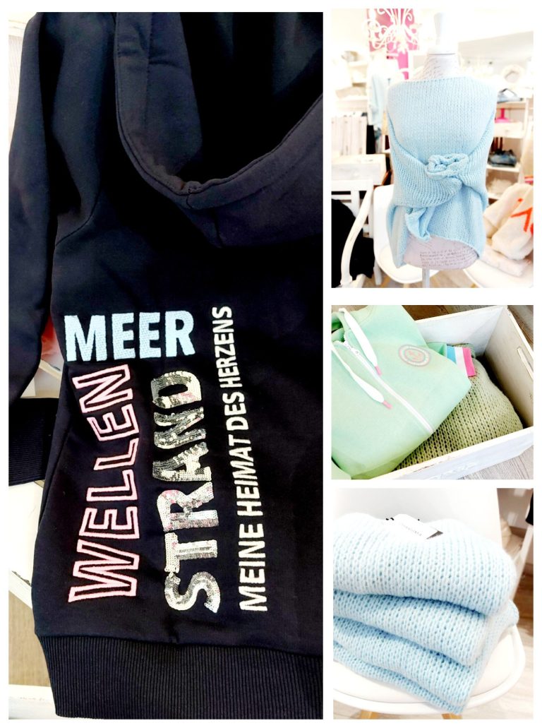 Text auf Kleidung: "Meer Wellen Strand - Meine Heimat des Lebens". Farbenfrohe Kleidung auf einem Tisch.