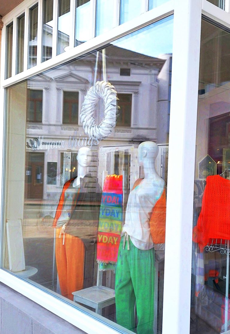 Schaufenster mit bunten Kleidungsstücken und dekoriertem Kranz.