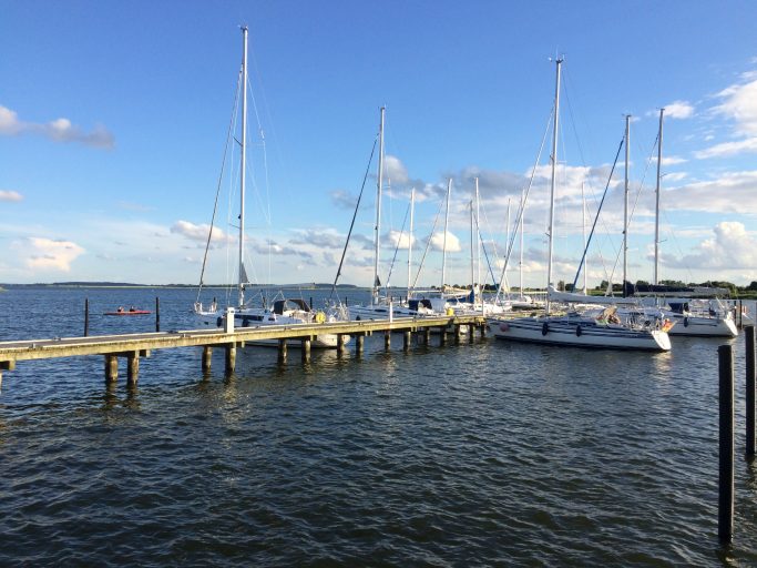 Hafen mit Segelbooten und Steg unter blauem Himmel und leicht bewölktem Wetter.