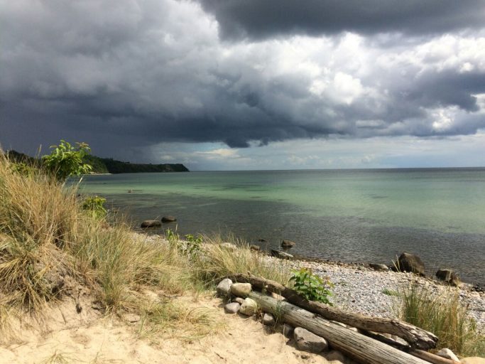 Dünenlandschaft am Meer unter bewölktem Himmel, mit ruhigem Wasser.